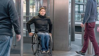 Ein Rollstuhlfahrer fährt aus einem Aufzug an einem Bahnhof