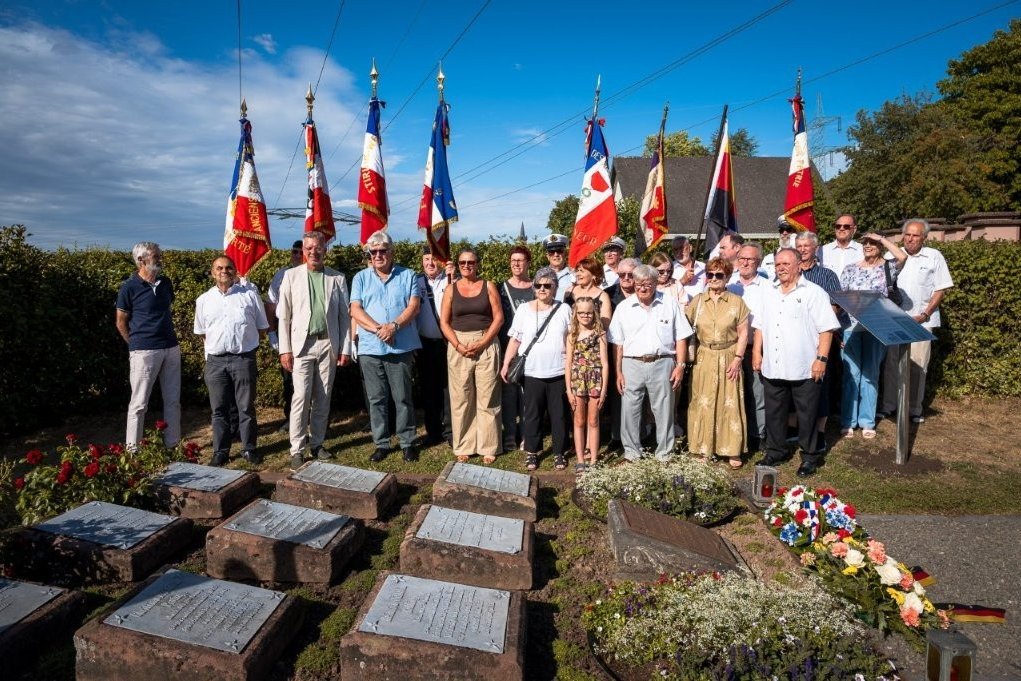 Eine Gruppe von Menschen mit Fahnen stehen vor einem Kriegsgräber-Denkmal auf dem Friedhof in Elversberg.